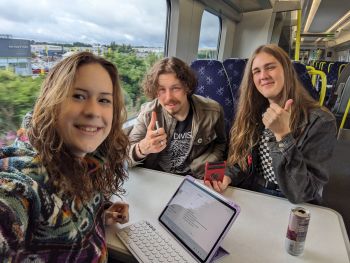 Skye, Jon, and Luna on a train, taking a selfie with smiles and thumbs up