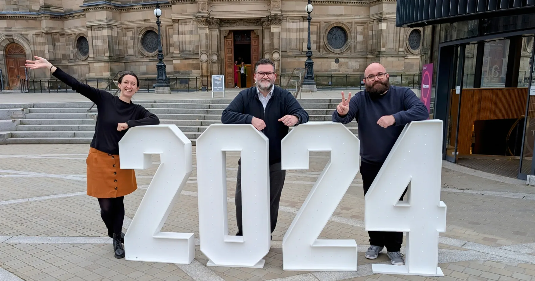 ECSA Staff Team of Genevieve, Al, and Graham, standing behind the numbers 2024 at Graduation 2024