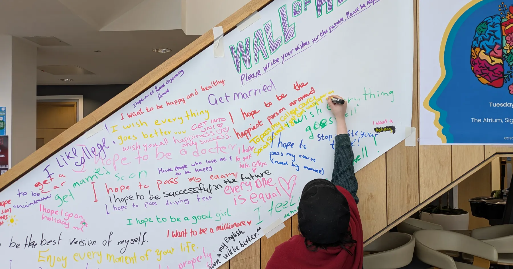 a woman writing on a 'wall of hope' banner at an event at Sighthill campus