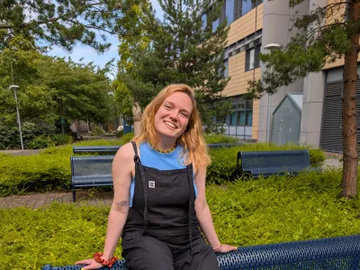 Woman sits on the back of a bench wearing dungarees.